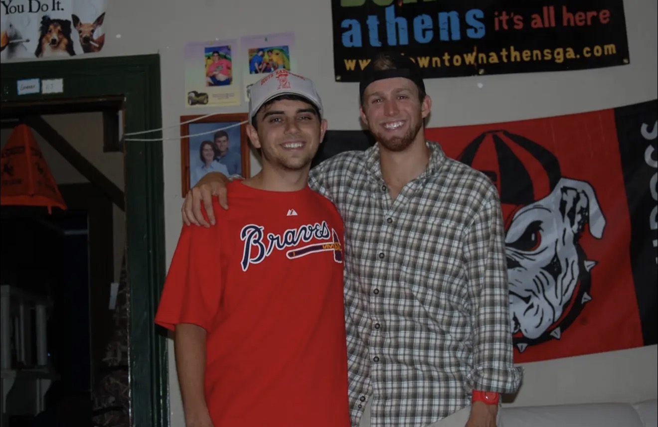 Two guys laughing in the living room under an Athens banner